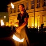 Detlef Vogt führt eine Feuershow auf, indem sie nachts vor einem wunderschön beleuchteten Gebäude mit brennenden Fackeln jongliert und so für eine unvergessliche Hochzeitsfeier sorgt.