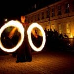 Feuerkünstler lässt nachts zwei brennende Fackeln vor einem Gebäude kreisen und begeistert das Publikum während einer Hochzeitsfeier mit einer unglaublichen Feuershow.