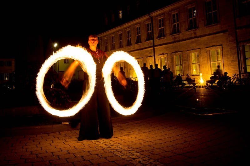 Feuerkünstler lässt nachts zwei brennende Fackeln vor einem Gebäude kreisen und begeistert das Publikum während einer Hochzeitsfeier mit einer unglaublichen Feuershow.