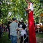 Gaukler auf Stelzen mit Hundemarionette vor einem Jungen