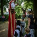 Mittelaltergaukler mit Hundemarionette auf Stelzen vor Kinden