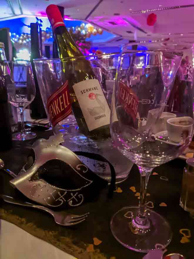 Ein gedeckter Tisch an Silvester mit Weingläsern und einer Flasche Wein und einer venezianischen Maske