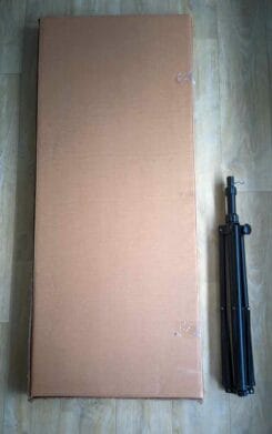 Brennendes Herz zur Vermietung verpackt im Karton liegt neben einem zusammengeklappten schwarzen Stativ auf einem Holzboden.