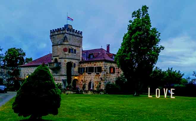 Schloss Geyersberg bei Coburg, umgeben von grünem Rasen und Bäumen. Auf der rechten Bildseite leuchtet in großen Lettern „LOVE“.